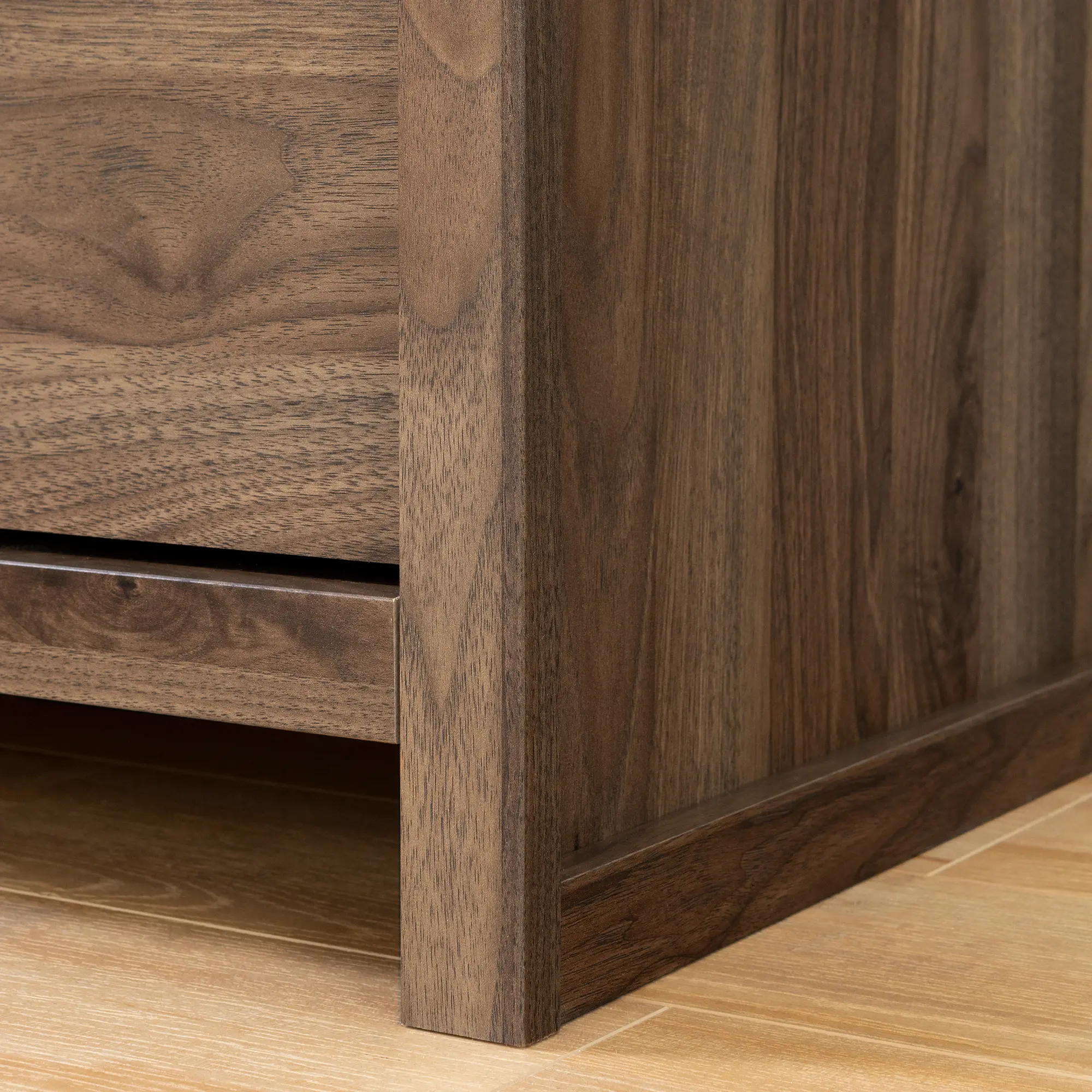 Close-up of wood grain and the edge of a nightstand drawer front and base.