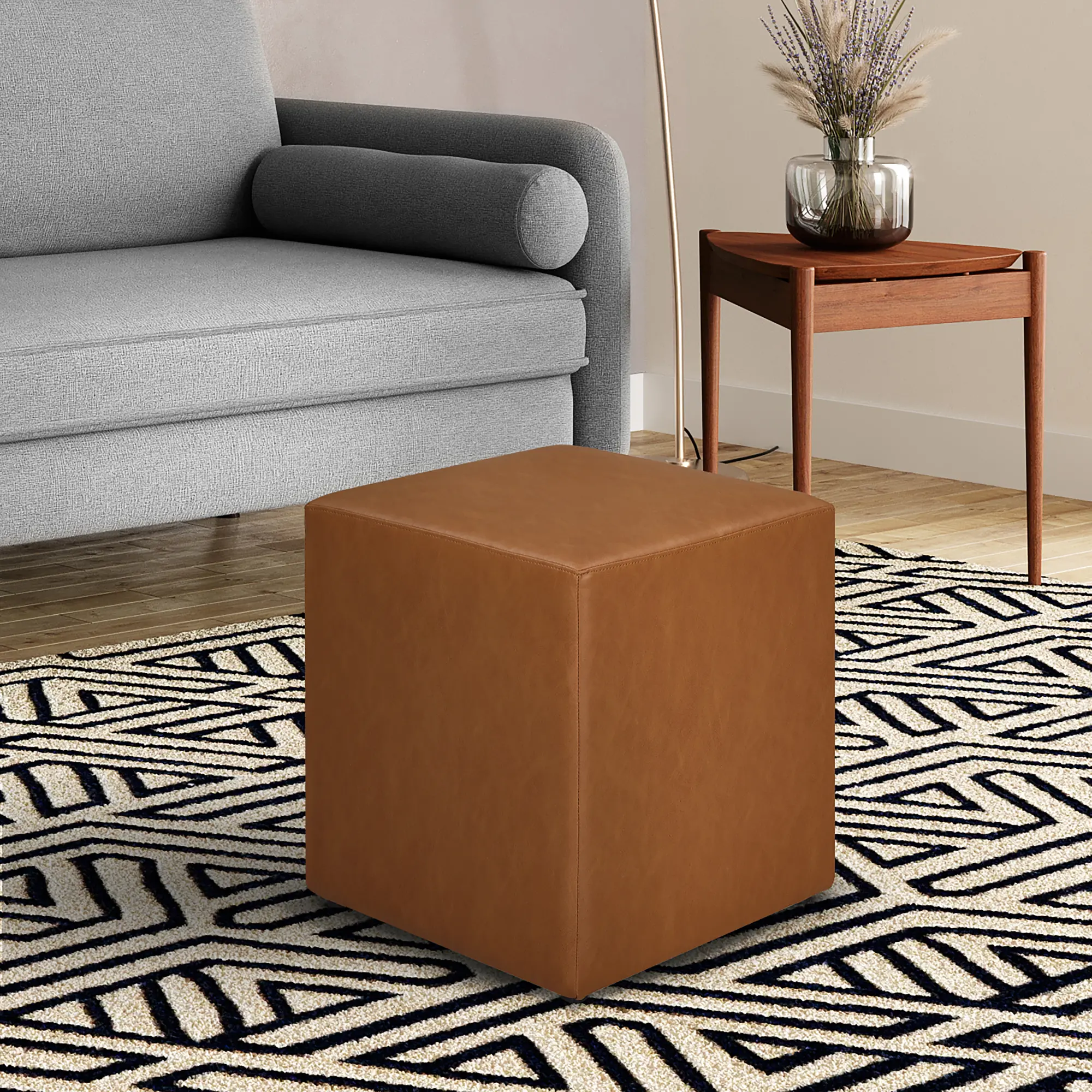 A square brown leather ottoman in a living room setting with a gray sofa and side table