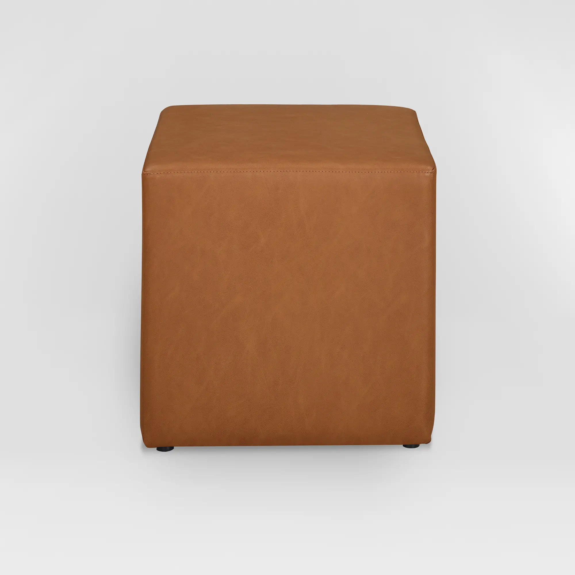Front-facing view of a brown leather ottoman showing its cube shape and stitched edges