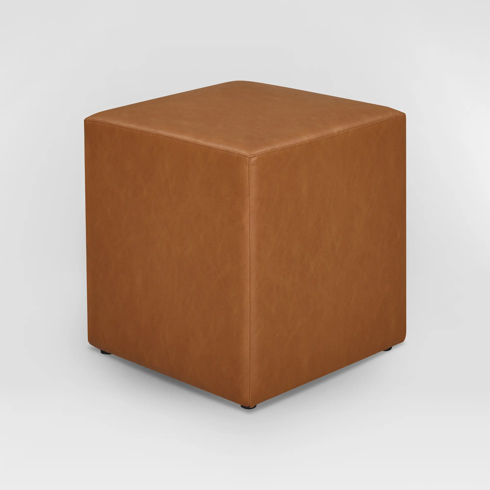 Three-quarter view of a brown leather ottoman against a neutral backdrop