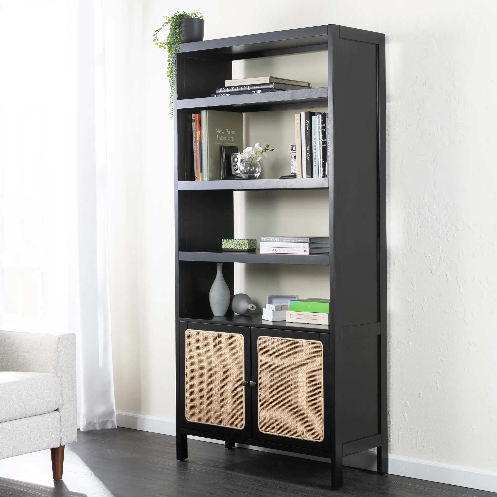 Tall black bookshelf unit with woven rattan cabinet doors at bottom, displayed in a living room