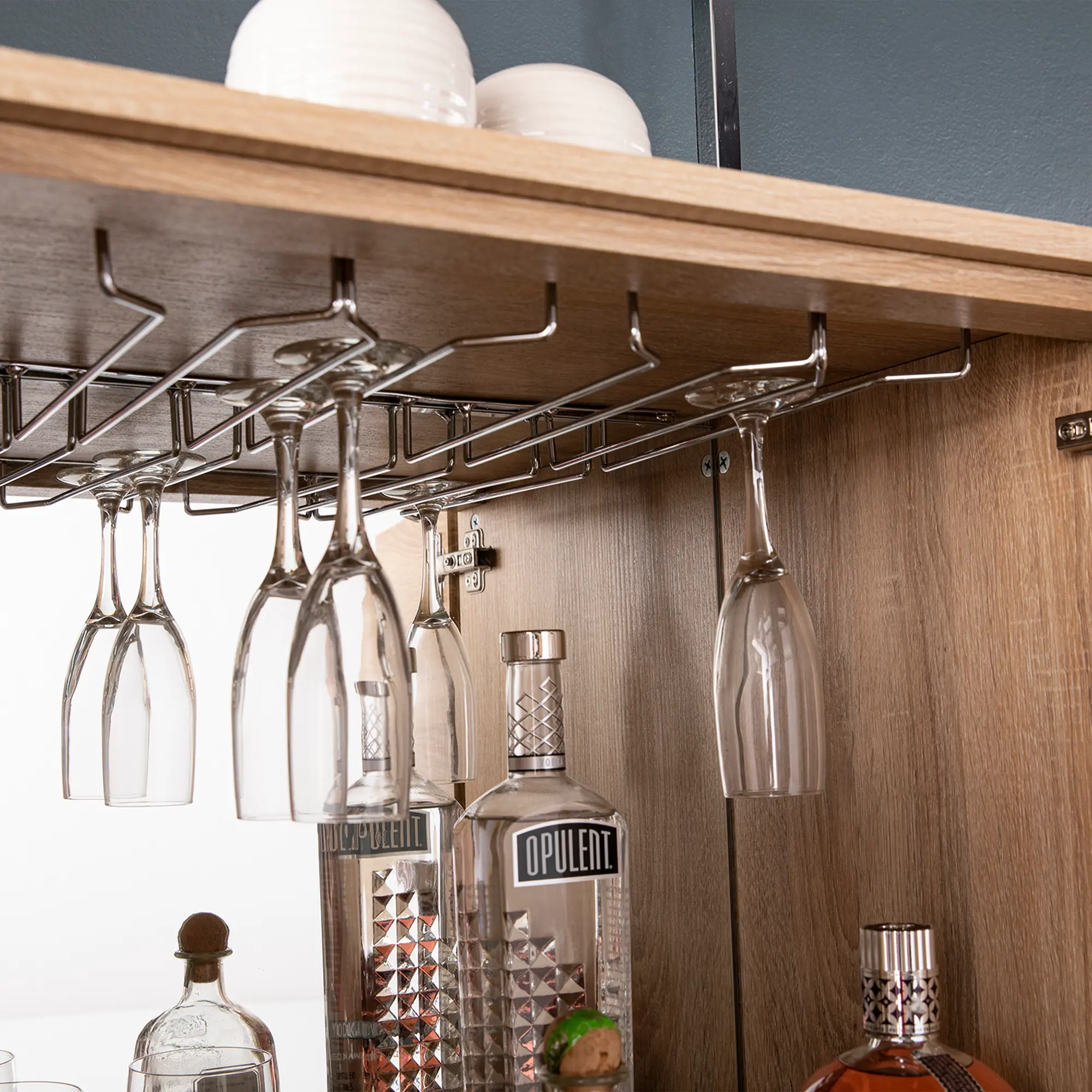 Close-up of hanging glass racks under a wooden shelf with glasses and a bottle beneath.